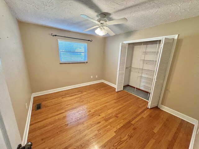 unfurnished bedroom with a textured ceiling, a closet, hardwood / wood-style flooring, and ceiling fan