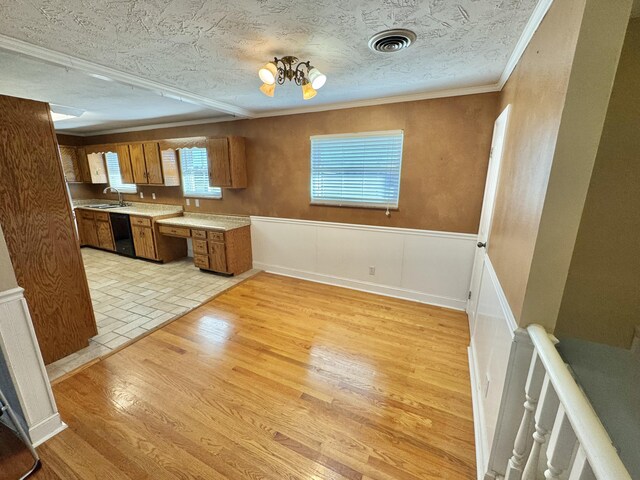 kitchen with sink, black dishwasher, light wood-type flooring, a textured ceiling, and ornamental molding