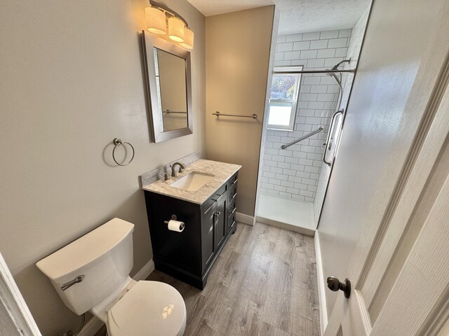 bathroom with vanity, toilet, a tile shower, and wood-type flooring