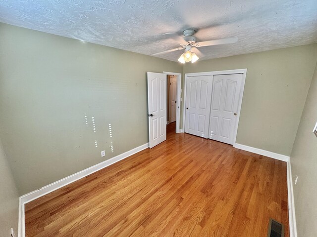 unfurnished bedroom with ceiling fan, a closet, light hardwood / wood-style floors, and a textured ceiling