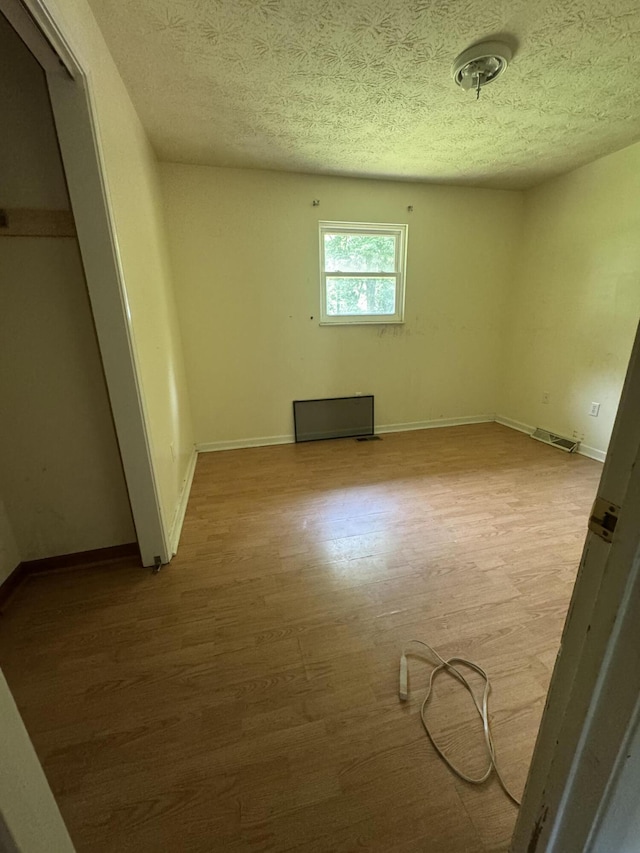 unfurnished bedroom featuring light wood-type flooring, baseboards, a textured ceiling, and a closet