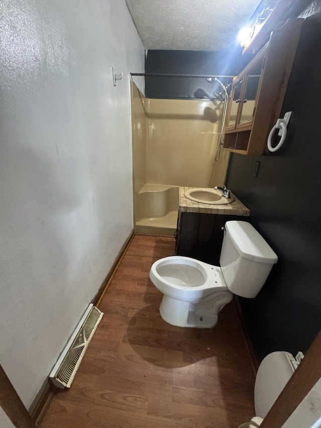 full bathroom with toilet, a sink, wood finished floors, a walk in shower, and a textured ceiling