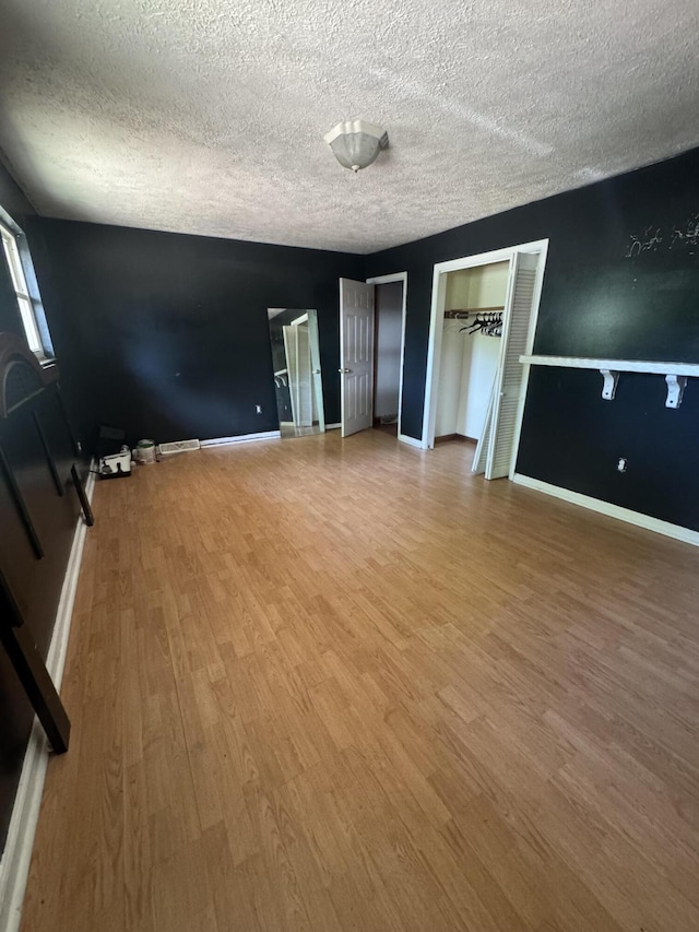 unfurnished bedroom with wood finished floors, a textured ceiling, two closets, and baseboards