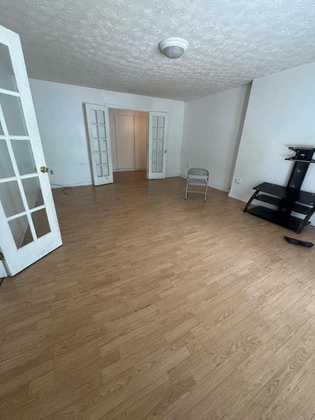 empty room with french doors, wood finished floors, a textured ceiling, and baseboards