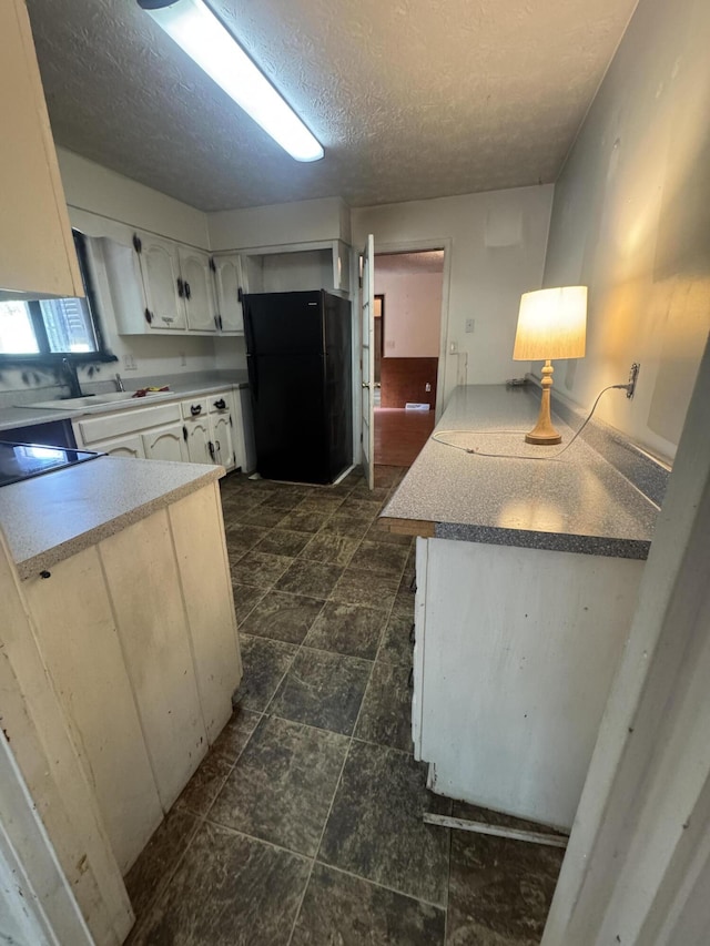 kitchen with freestanding refrigerator, white cabinets, a textured ceiling, and a sink