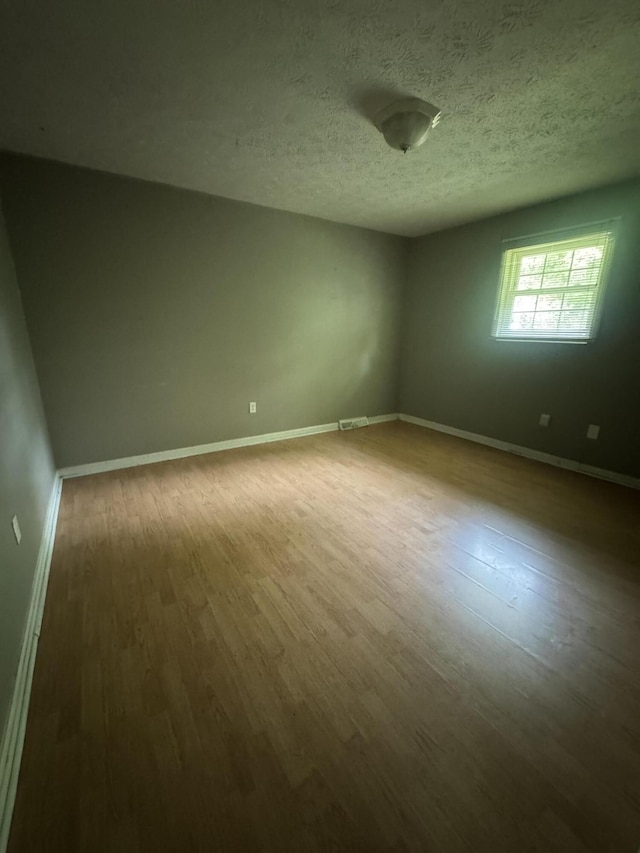 empty room featuring wood finished floors, baseboards, and a textured ceiling