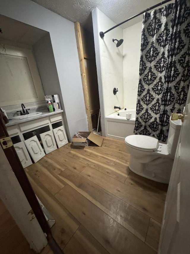 bathroom with hardwood / wood-style flooring, a textured ceiling, shower / bath combo, toilet, and vanity