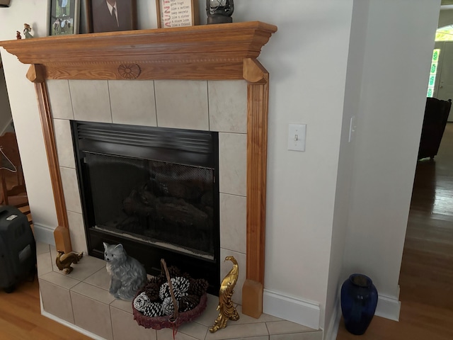 detailed view of a tiled fireplace, wood finished floors, and baseboards
