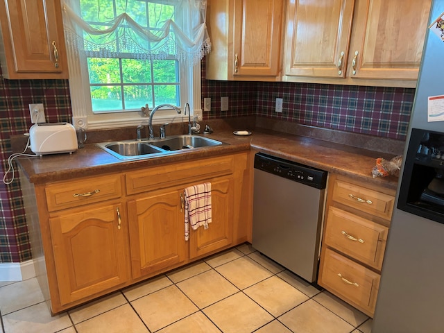 kitchen with appliances with stainless steel finishes, a sink, light tile patterned floors, backsplash, and dark countertops