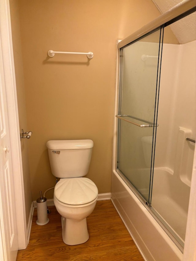 bathroom featuring hardwood / wood-style flooring, shower / bath combination with glass door, toilet, and a textured ceiling