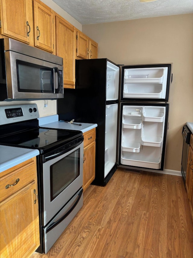 kitchen with light wood-type flooring, a textured ceiling, and appliances with stainless steel finishes