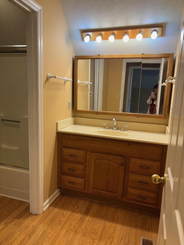 bathroom featuring vanity, combined bath / shower with glass door, hardwood / wood-style floors, and a textured ceiling