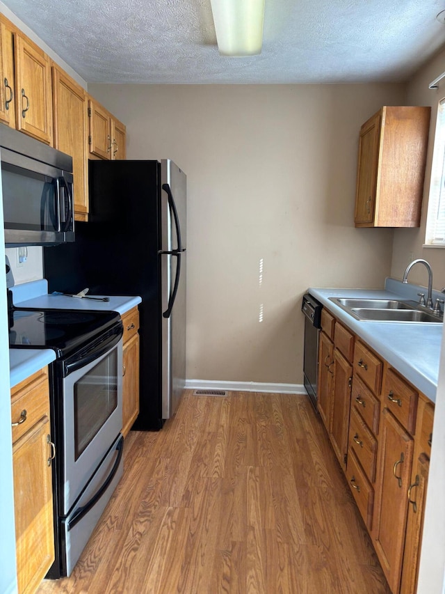 kitchen featuring appliances with stainless steel finishes, sink, a textured ceiling, and light hardwood / wood-style floors