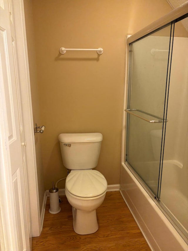 bathroom with combined bath / shower with glass door, hardwood / wood-style floors, and toilet