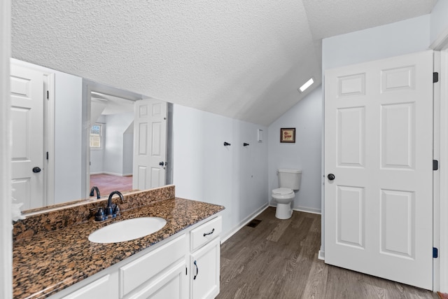 bathroom featuring vaulted ceiling, hardwood / wood-style flooring, vanity, toilet, and a textured ceiling