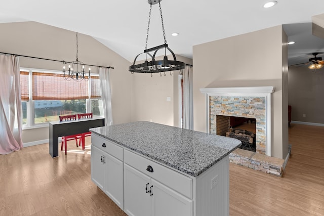 kitchen with white cabinetry, a center island, light wood-type flooring, pendant lighting, and light stone countertops