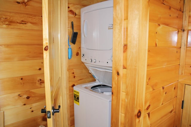 washroom featuring stacked washer and clothes dryer and wood walls