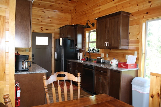 kitchen featuring dark brown cabinetry, vaulted ceiling, wood walls, and black appliances