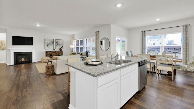 kitchen featuring a sink, dishwasher, light stone countertops, a center island with sink, and dark wood-type flooring