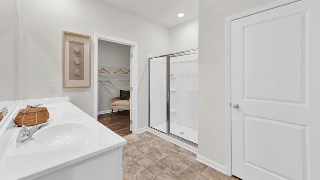 full bath with a shower stall, a spacious closet, baseboards, double vanity, and recessed lighting