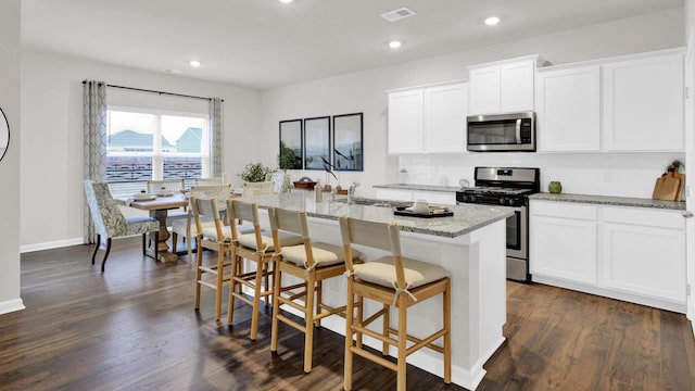 kitchen featuring stainless steel appliances, an island with sink, decorative backsplash, light stone countertops, and white cabinets