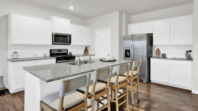 kitchen with appliances with stainless steel finishes, a sink, backsplash, a breakfast bar, and white cabinetry