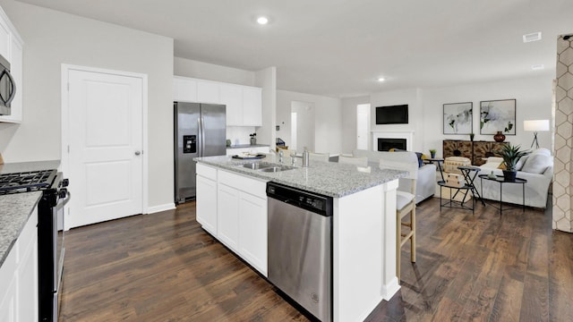 kitchen with appliances with stainless steel finishes, open floor plan, a sink, a fireplace, and a center island with sink