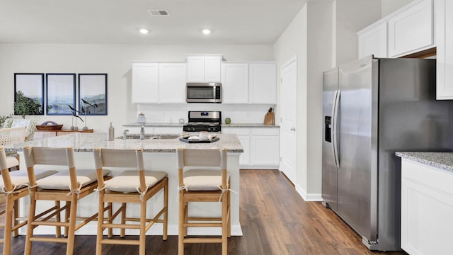kitchen with appliances with stainless steel finishes, a sink, light stone countertops, white cabinets, and recessed lighting