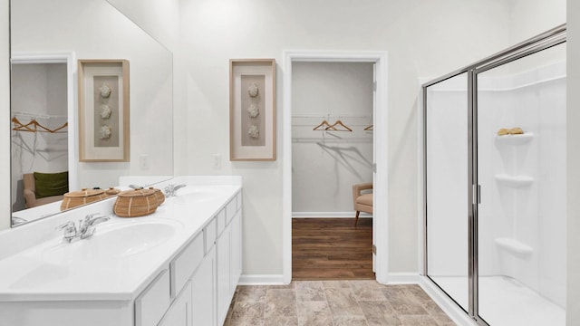 bathroom with a stall shower, double vanity, a walk in closet, and baseboards