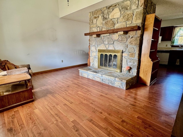 unfurnished living room featuring wood-type flooring, a stone fireplace, sink, and a textured ceiling