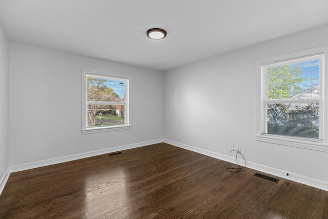 spare room with visible vents, plenty of natural light, and dark wood finished floors
