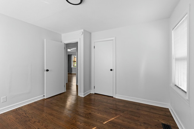 unfurnished bedroom featuring baseboards, multiple windows, dark wood-style floors, and visible vents