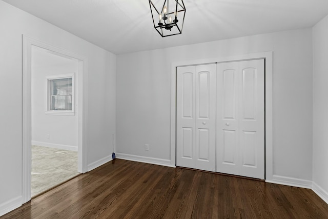 unfurnished bedroom featuring dark wood-style flooring, a closet, baseboards, and an inviting chandelier