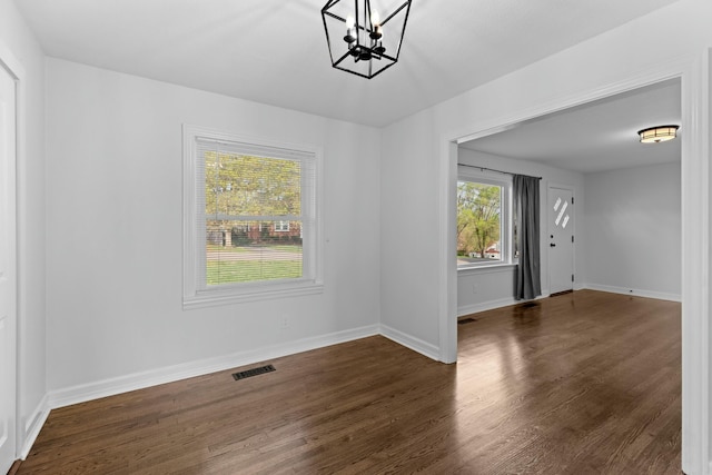 unfurnished dining area with visible vents, baseboards, an inviting chandelier, and wood finished floors
