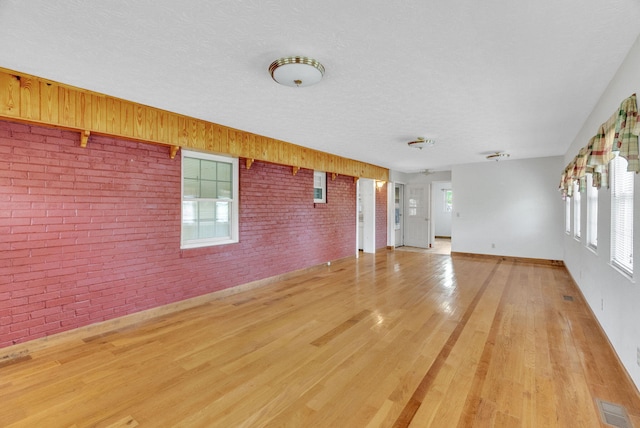 unfurnished living room with light hardwood / wood-style floors, a textured ceiling, and brick wall