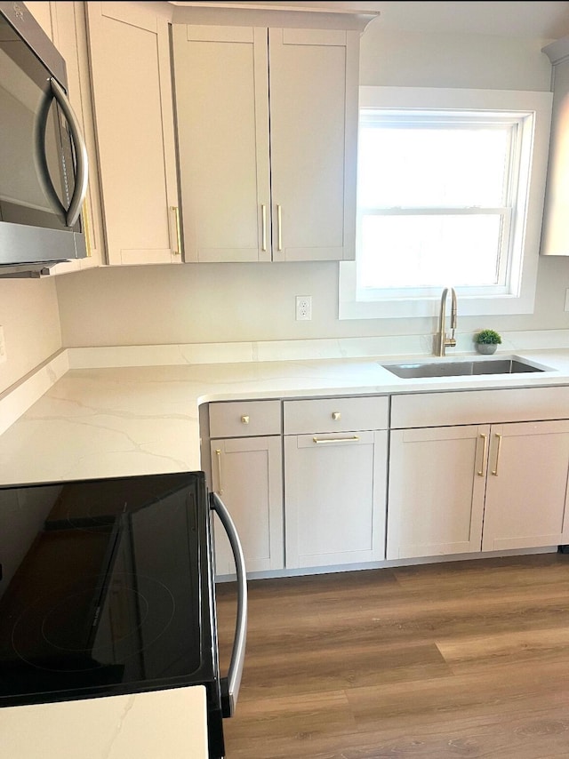 kitchen featuring light stone countertops, sink, stove, wood-type flooring, and white cabinets