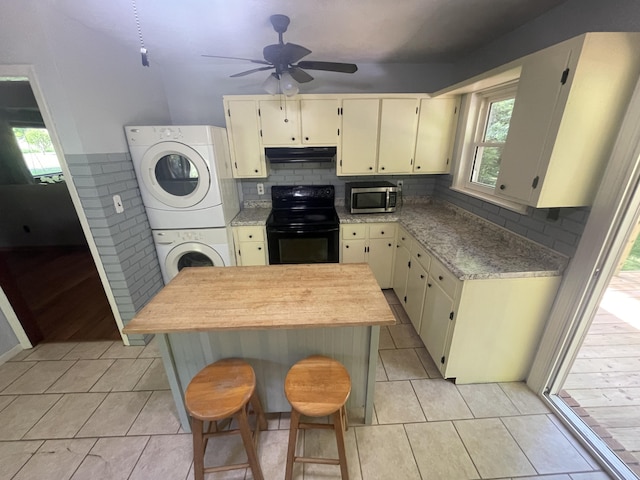 4124 Big Creek Rd, Hartford, TN 37753 - kitchen with black range with electric cooktop, stainless steel microwave, stacked washing machine and dryer, under cabinet range hood, and cream cabinetry
