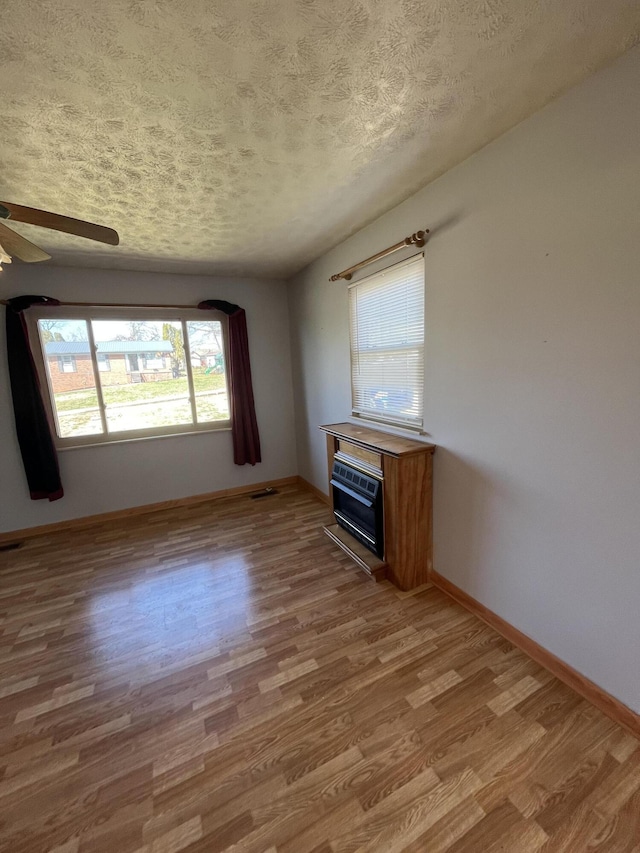 unfurnished living room featuring a textured ceiling, baseboards, and wood finished floors