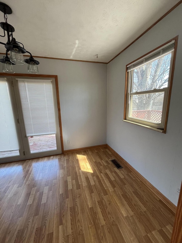 unfurnished room featuring a textured ceiling, wood finished floors, visible vents, baseboards, and ornamental molding