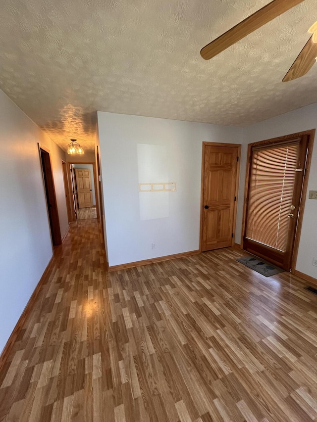 unfurnished room featuring a textured ceiling, ceiling fan, wood finished floors, and baseboards