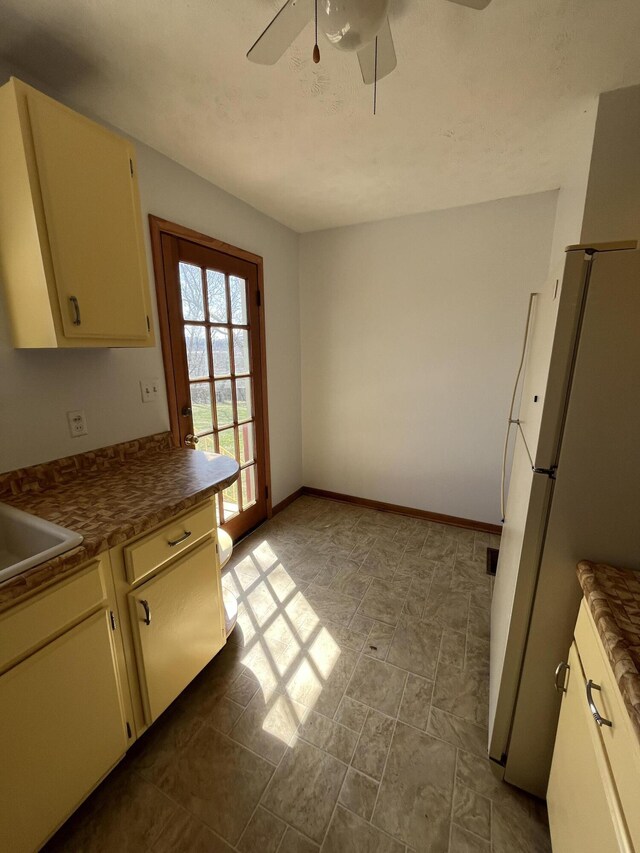 kitchen with baseboards, a ceiling fan, dark countertops, freestanding refrigerator, and cream cabinets