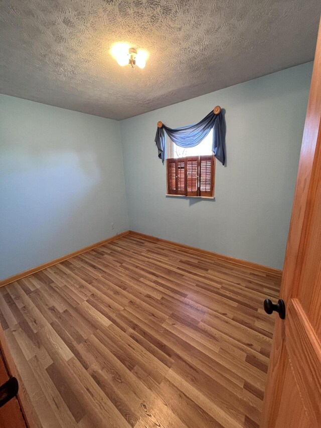 unfurnished room with a textured ceiling, wood finished floors, and baseboards