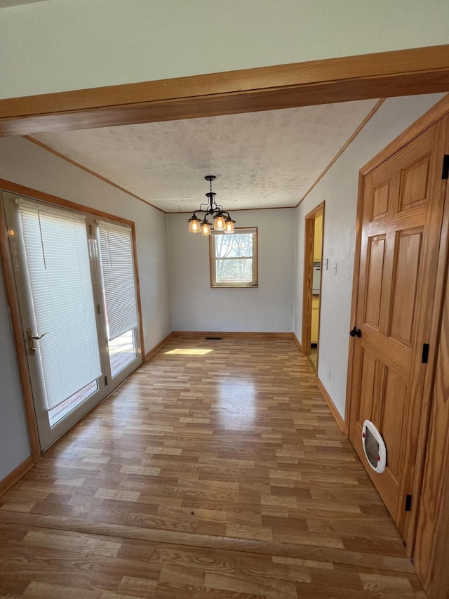 unfurnished dining area featuring light wood-type flooring, an inviting chandelier, baseboards, and crown molding