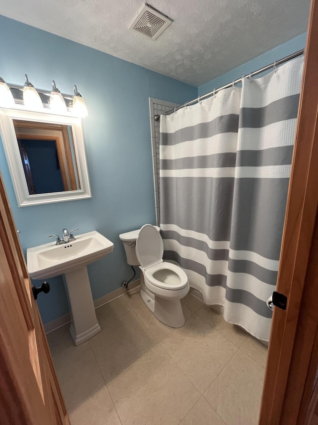 full bathroom featuring visible vents, toilet, a sink, a textured ceiling, and tile patterned floors