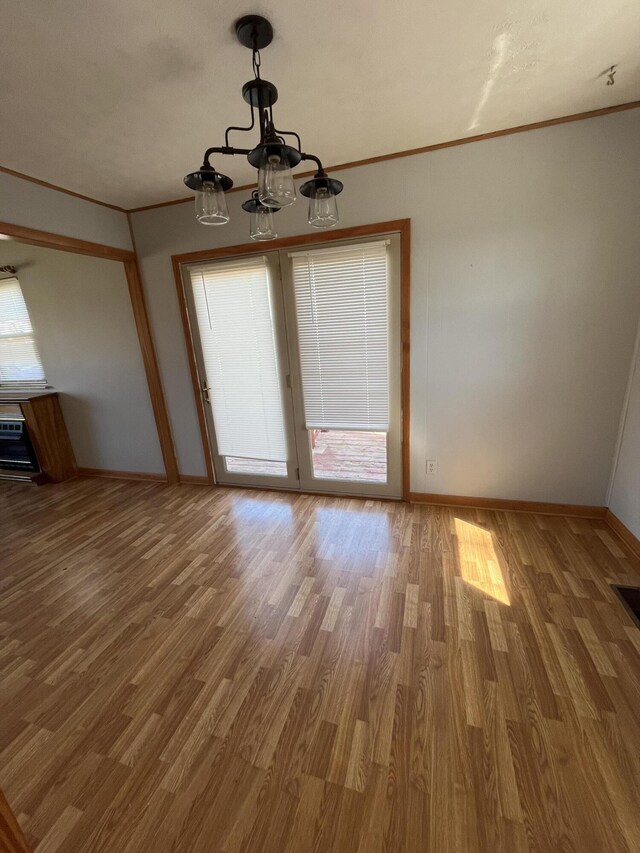 unfurnished dining area featuring baseboards, a chandelier, crown molding, and wood finished floors