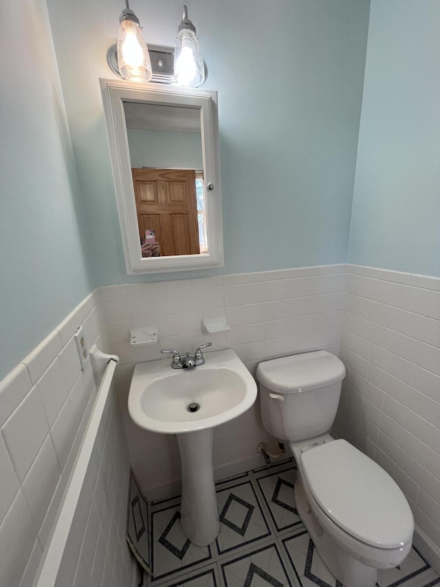 bathroom featuring a wainscoted wall, toilet, and tile walls