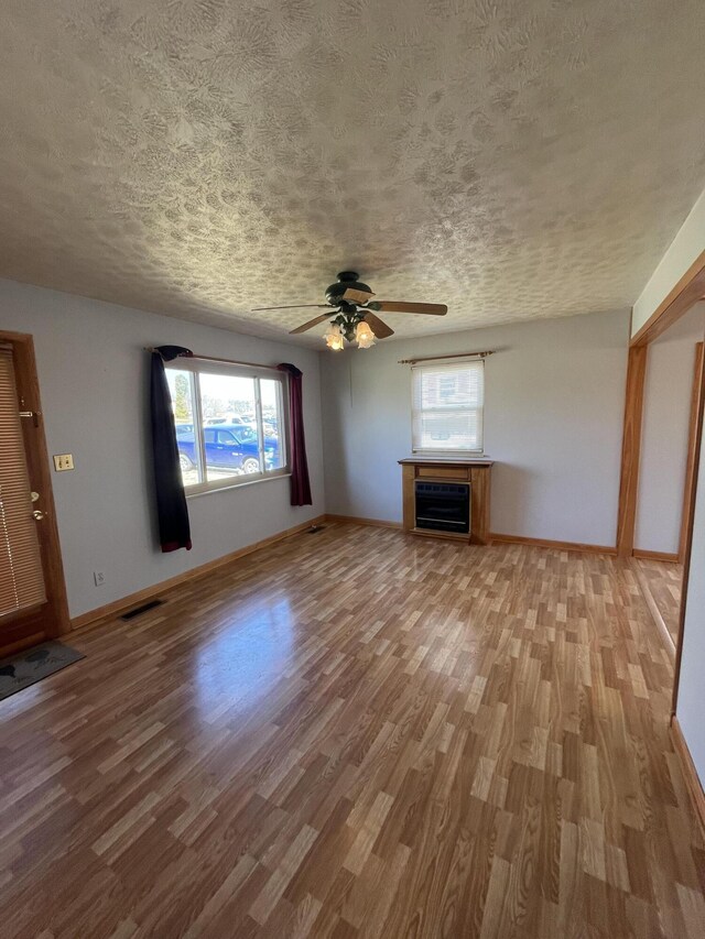 unfurnished living room with a fireplace, visible vents, a textured ceiling, wood finished floors, and baseboards