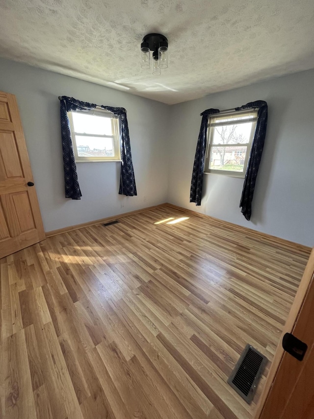 spare room featuring a textured ceiling, visible vents, and light wood-style floors