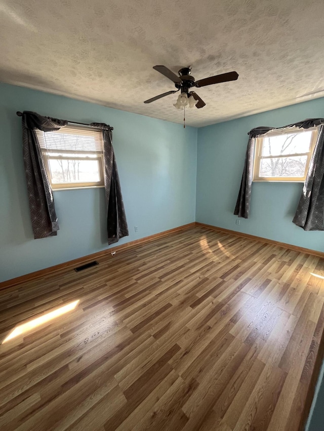 spare room with visible vents, plenty of natural light, a textured ceiling, and wood finished floors