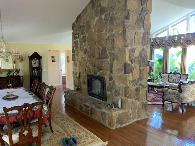 dining area with high vaulted ceiling, a stone fireplace, and hardwood / wood-style flooring